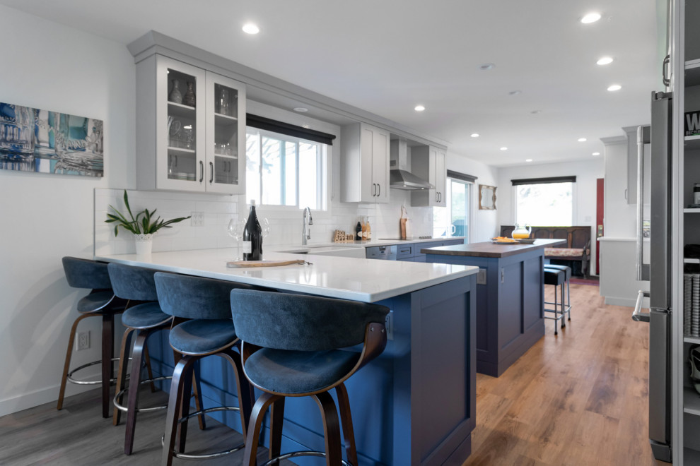 Mid-sized transitional u-shaped medium tone wood floor and brown floor eat-in kitchen photo with recessed-panel cabinets, gray cabinets, quartz countertops, white backsplash, ceramic backsplash, stainless steel appliances, an island and white countertops