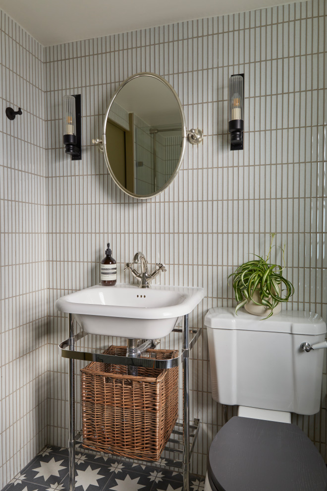 Small transitional powder room in London with open cabinets, a two-piece toilet, white tile, matchstick tile, cement tiles, black floor, a freestanding vanity and a console sink.
