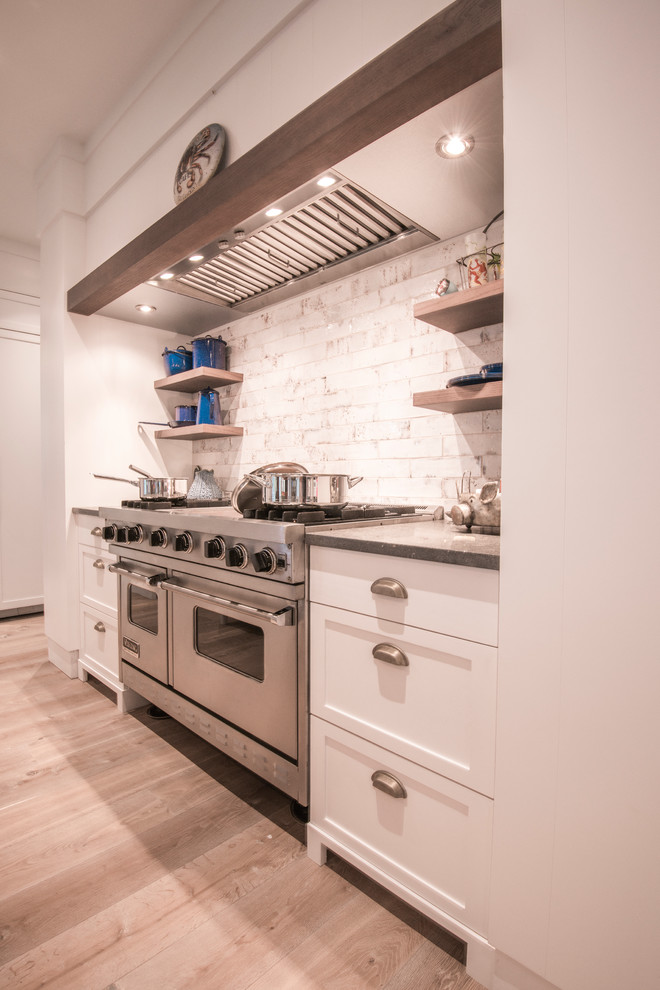 Photo of a mid-sized eclectic u-shaped open plan kitchen in Tampa with an undermount sink, shaker cabinets, white cabinets, limestone benchtops, white splashback, subway tile splashback, panelled appliances, light hardwood floors, with island, beige floor and grey benchtop.