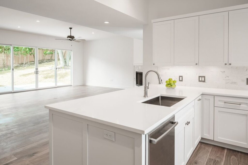Transitional u-shaped medium tone wood floor enclosed kitchen photo in Austin with a single-bowl sink, shaker cabinets, white cabinets, quartz countertops, white backsplash, stone tile backsplash, stainless steel appliances and a peninsula