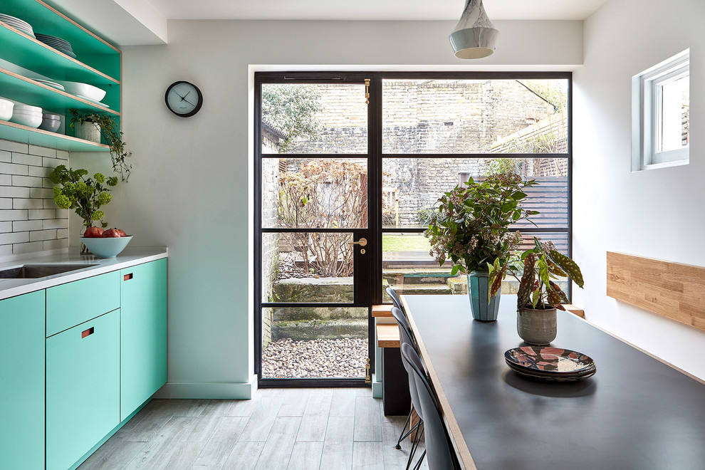 Photo of a mid-sized scandinavian l-shaped eat-in kitchen in London with an undermount sink, flat-panel cabinets, turquoise cabinets, solid surface benchtops, white splashback, subway tile splashback, panelled appliances, porcelain floors, no island, grey floor and white benchtop.