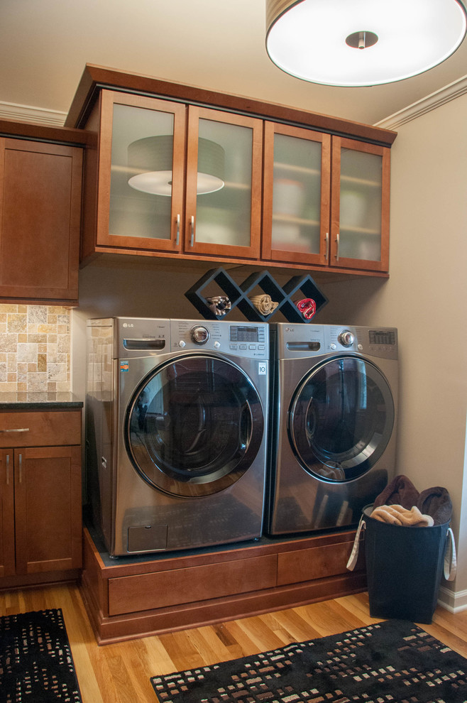 Inspiration for a mid-sized traditional u-shaped dedicated laundry room in Kansas City with an undermount sink, shaker cabinets, medium wood cabinets, granite benchtops, beige walls, medium hardwood floors and a side-by-side washer and dryer.