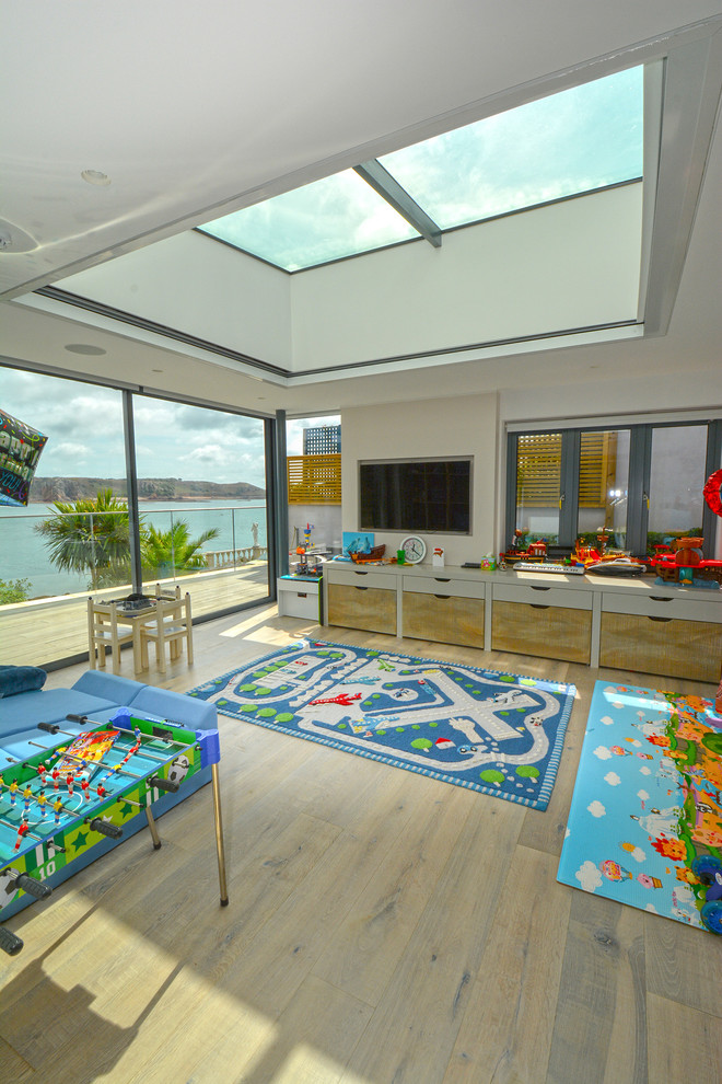 Large contemporary gender-neutral kids' room in Channel Islands with white walls, light hardwood floors and beige floor.