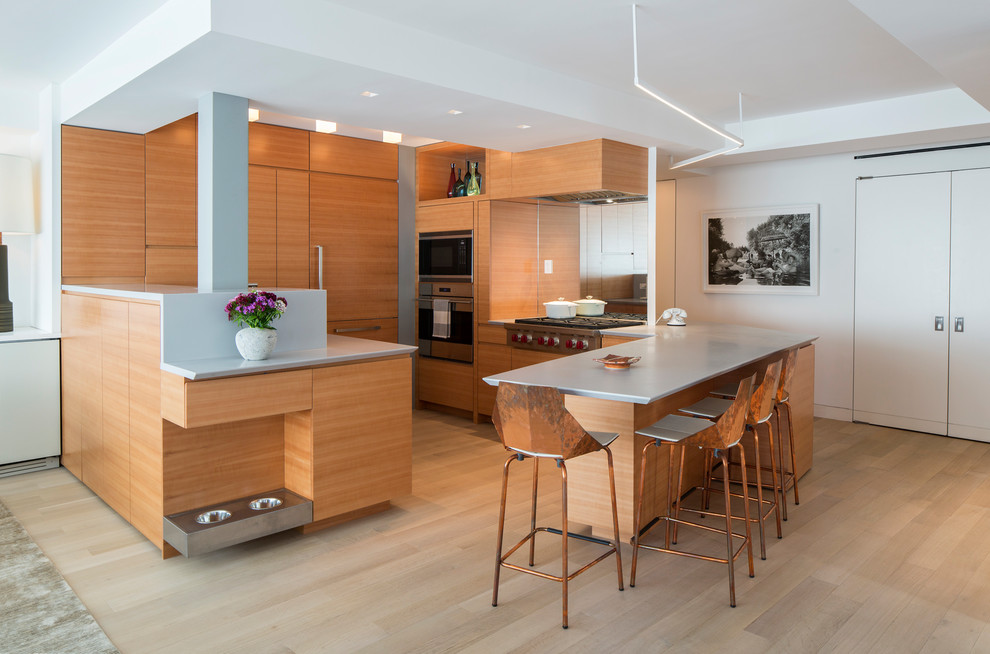 Photo of a contemporary u-shaped kitchen in New York with flat-panel cabinets, medium wood cabinets, mirror splashback, stainless steel appliances, light hardwood floors, a peninsula and beige floor.