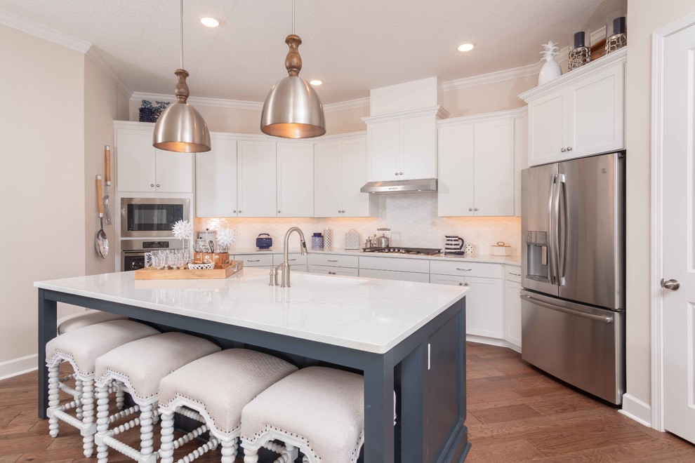 Photo of a beach style kitchen in Jacksonville with an undermount sink, shaker cabinets, white cabinets, white splashback, stainless steel appliances, medium hardwood floors, with island and white benchtop.