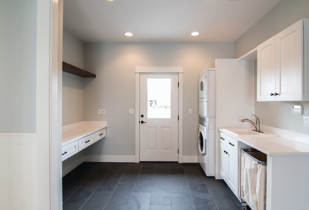 Inspiration for a large arts and crafts galley utility room in Other with a drop-in sink, shaker cabinets, white cabinets, quartz benchtops, blue walls, slate floors, a stacked washer and dryer and beige floor.