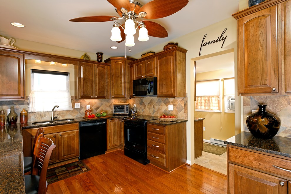 Eat-in kitchen - transitional l-shaped eat-in kitchen idea in DC Metro with a double-bowl sink, furniture-like cabinets, medium tone wood cabinets, granite countertops, beige backsplash, mosaic tile backsplash and black appliances