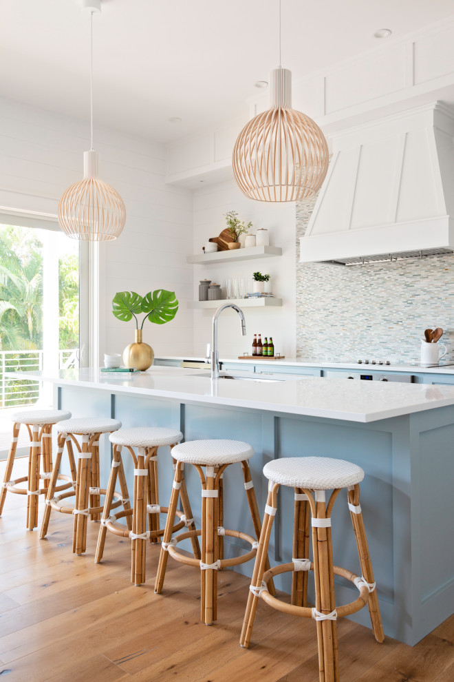 Photo of a large beach style galley kitchen in Tampa with an undermount sink, shaker cabinets, blue cabinets, multi-coloured splashback, matchstick tile splashback, medium hardwood floors, with island, beige floor and white benchtop.