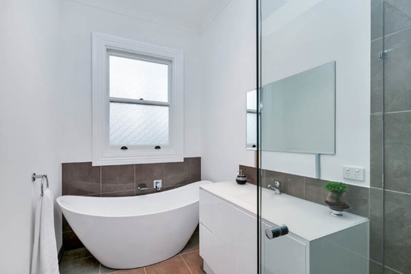 Inspiration for a mid-sized contemporary master bathroom in Other with beaded inset cabinets, white cabinets, a freestanding tub, a corner shower, a one-piece toilet, white tile, porcelain tile, white walls, porcelain floors, an integrated sink, engineered quartz benchtops, brown floor, a hinged shower door and white benchtops.