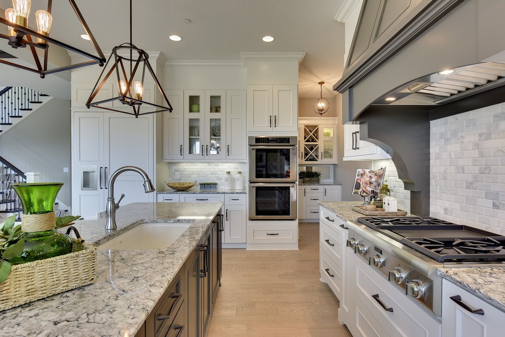 Large transitional light wood floor and beige floor open concept kitchen photo in Minneapolis with an undermount sink, white cabinets, quartz countertops, white backsplash, marble backsplash, stainless steel appliances and an island