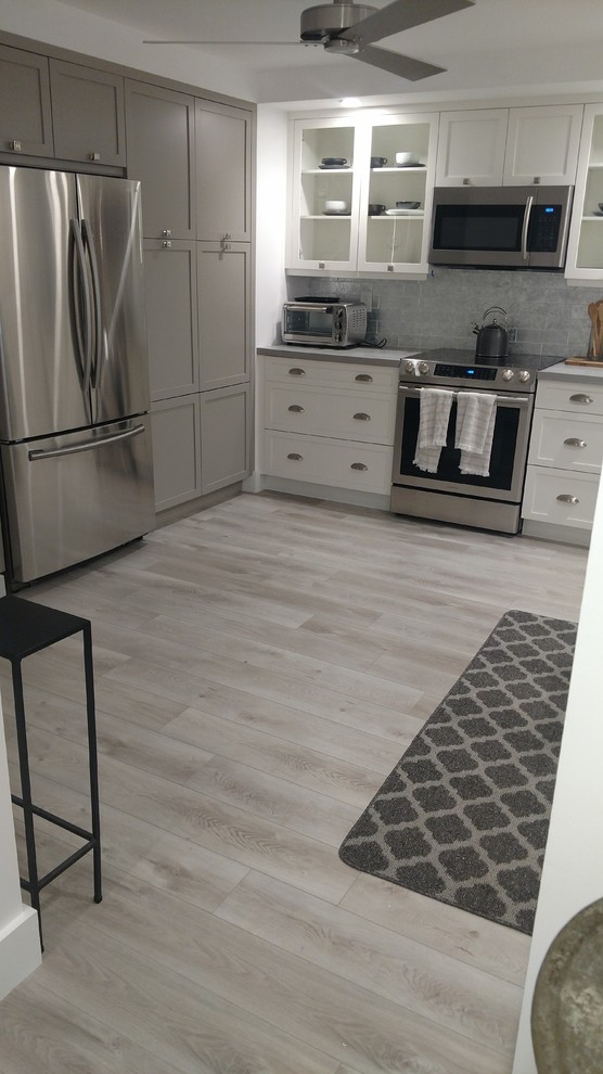 Example of a large transitional u-shaped dark wood floor and gray floor enclosed kitchen design in Miami with an undermount sink, shaker cabinets, white cabinets, quartz countertops, white backsplash, stainless steel appliances, an island and white countertops