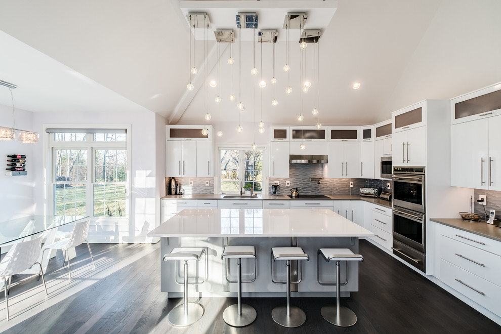 Large contemporary l-shaped eat-in kitchen in Bridgeport with an undermount sink, flat-panel cabinets, white cabinets, quartz benchtops, stainless steel appliances, dark hardwood floors, with island, grey splashback, brown floor, grey benchtop and glass tile splashback.