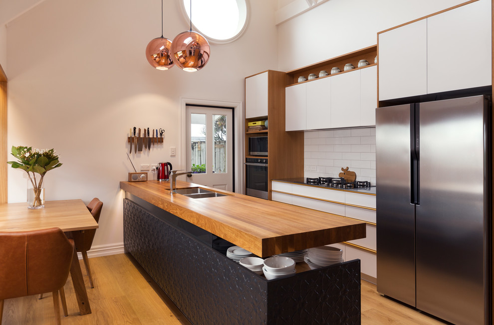 Photo of a contemporary galley eat-in kitchen in Other with a double-bowl sink, flat-panel cabinets, white cabinets, white splashback, subway tile splashback, stainless steel appliances, medium hardwood floors and with island.
