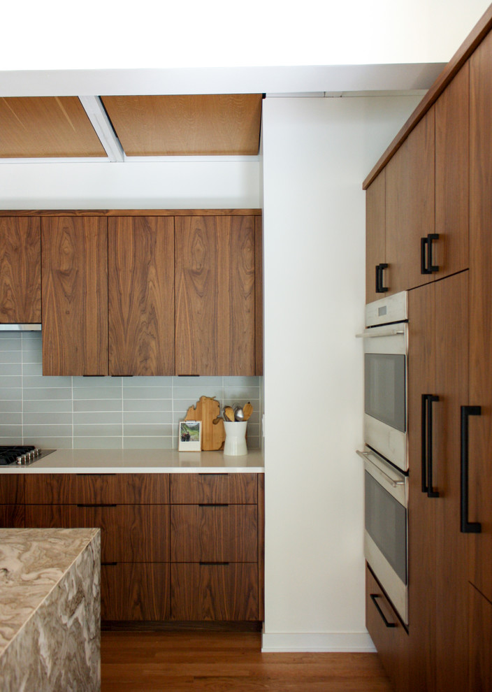 Photo of a mid-sized midcentury single-wall eat-in kitchen in Detroit with a drop-in sink, flat-panel cabinets, medium wood cabinets, quartzite benchtops, grey splashback, ceramic splashback, stainless steel appliances, medium hardwood floors, with island, orange floor and beige benchtop.