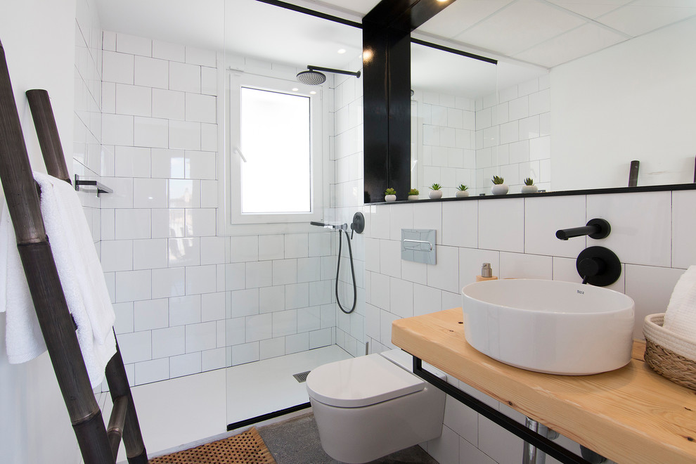 This is an example of a beach style 3/4 bathroom in Madrid with an alcove shower, a wall-mount toilet, white tile, white walls, concrete floors, a vessel sink, wood benchtops, grey floor, an open shower and beige benchtops.