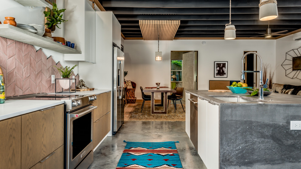 Mid-sized eclectic galley eat-in kitchen in Houston with an undermount sink, flat-panel cabinets, light wood cabinets, concrete benchtops, pink splashback, terra-cotta splashback, stainless steel appliances, concrete floors, with island, grey floor, exposed beam and grey benchtop.