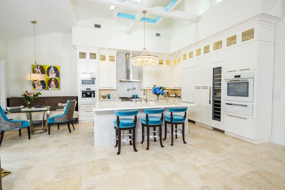 Expansive transitional l-shaped eat-in kitchen in Miami with a farmhouse sink, white cabinets, quartzite benchtops, white splashback, stone tile splashback, white appliances, travertine floors and with island.