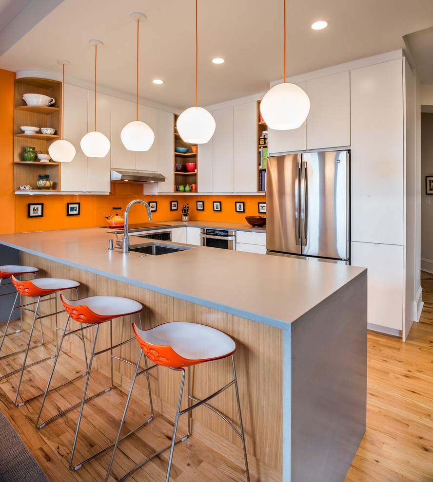 Contemporary u-shaped kitchen in Philadelphia with an undermount sink, flat-panel cabinets, white cabinets, orange splashback, stainless steel appliances, light hardwood floors and a peninsula.