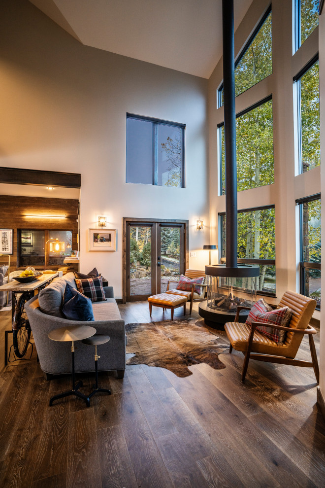 Example of a large mountain style open concept dark wood floor, vaulted ceiling and brown floor living room design in Denver with yellow walls and a hanging fireplace