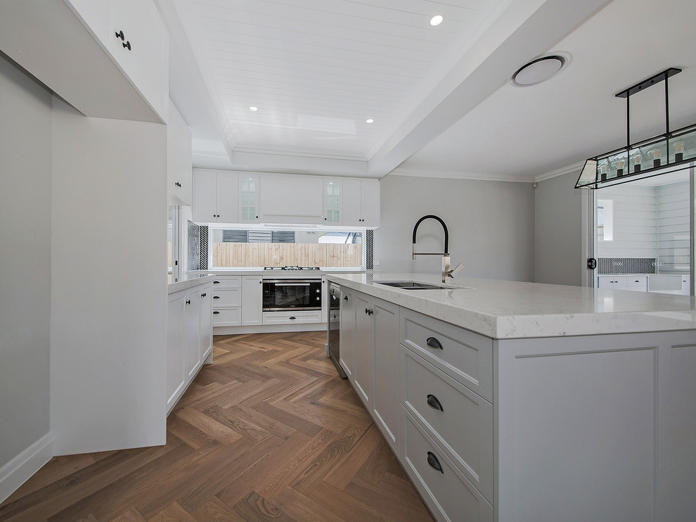 This is an example of a large traditional open plan kitchen in Brisbane with an undermount sink, shaker cabinets, grey cabinets, marble benchtops, black splashback, ceramic splashback, stainless steel appliances, medium hardwood floors, with island, brown floor and white benchtop.
