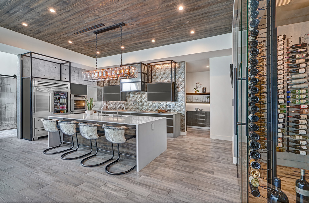 Inspiration for an expansive industrial l-shaped open plan kitchen in Sacramento with an undermount sink, grey cabinets, quartz benchtops, grey splashback, glass tile splashback, stainless steel appliances, light hardwood floors, with island, grey floor, white benchtop and flat-panel cabinets.