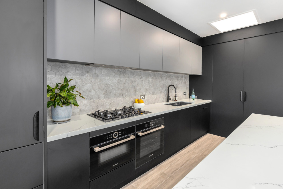 Design ideas for a mid-sized contemporary galley open plan kitchen in Melbourne with flat-panel cabinets, quartz benchtops, black appliances, porcelain floors, with island, a double-bowl sink, black cabinets, mosaic tile splashback and grey benchtop.