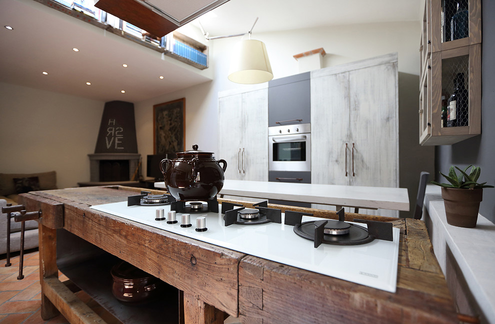 This is an example of a mid-sized industrial single-wall eat-in kitchen in Florence with an undermount sink, open cabinets, light wood cabinets, wood benchtops, red splashback, cement tile splashback, stainless steel appliances, terra-cotta floors and with island.