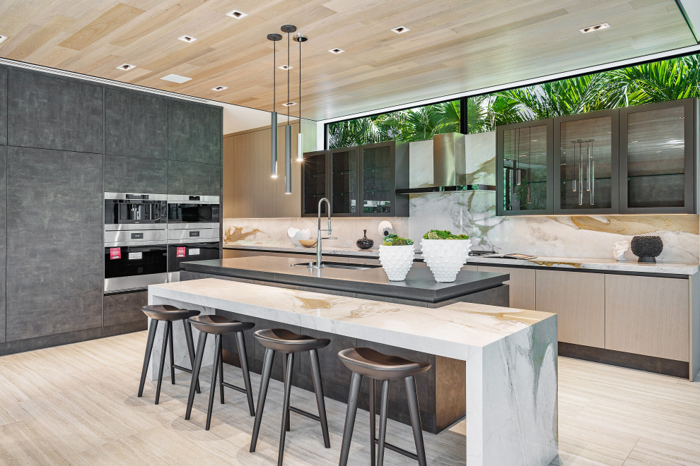 Photo of an expansive contemporary kitchen in Miami with glass-front cabinets, marble benchtops, black splashback, marble splashback, stainless steel appliances, porcelain floors, beige floor, beige benchtop, wood and with island.