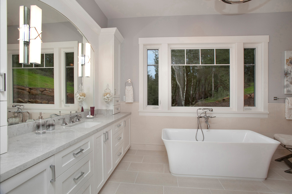Photo of a large transitional master bathroom in San Francisco with shaker cabinets, white cabinets, a freestanding tub, a two-piece toilet, beige tile, porcelain tile, grey walls, porcelain floors, an undermount sink and engineered quartz benchtops.