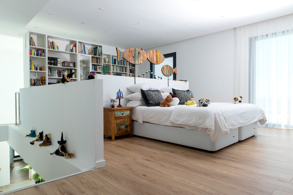 Photo of a large contemporary gender-neutral kids' room in Other with white walls, light hardwood floors and beige floor.