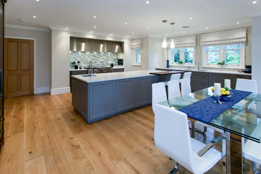 Photo of a large transitional l-shaped open plan kitchen in London with an undermount sink, recessed-panel cabinets, grey cabinets, solid surface benchtops, multi-coloured splashback, mosaic tile splashback, stainless steel appliances, light hardwood floors and with island.