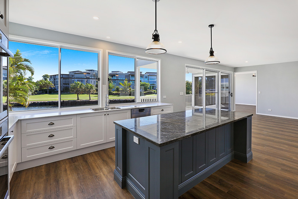 Photo of a large contemporary l-shaped eat-in kitchen in Sunshine Coast with a drop-in sink, shaker cabinets, white cabinets, marble benchtops, white splashback, subway tile splashback, stainless steel appliances, dark hardwood floors, with island, brown floor and multi-coloured benchtop.