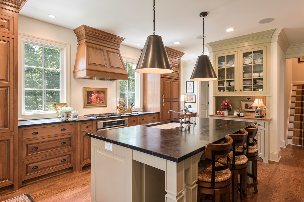 Open concept kitchen - mid-sized traditional l-shaped dark wood floor and brown floor open concept kitchen idea with an undermount sink, raised-panel cabinets, dark wood cabinets, soapstone countertops, stainless steel appliances and an island