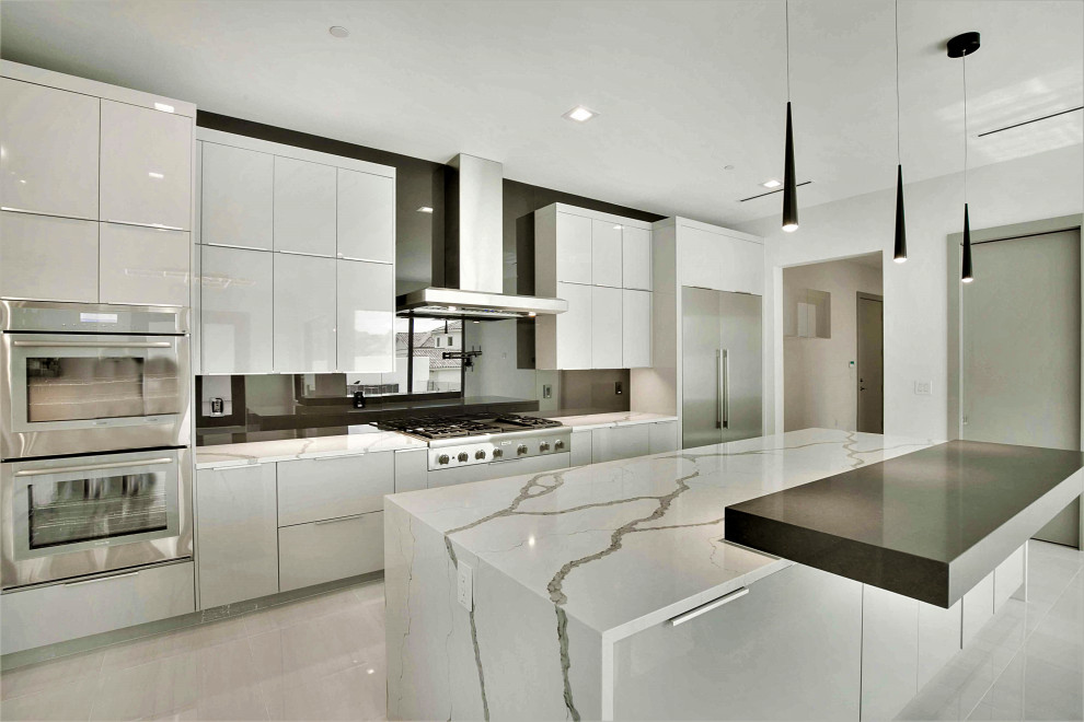 Inredning av ett modernt stort vit vitt l-kök, med en nedsänkt diskho, släta luckor, grå skåp, bänkskiva i kvarts, svart stänkskydd, glaspanel som stänkskydd, rostfria vitvaror, klinkergolv i porslin, en köksö och vitt golv