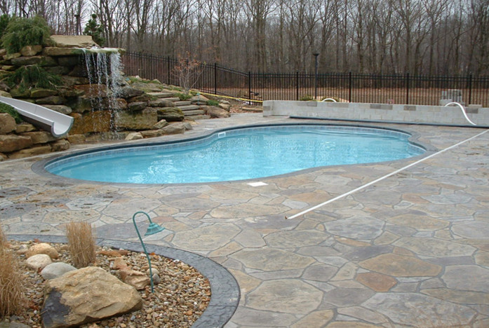 Mid-sized country backyard custom-shaped pool in Other with a water slide and natural stone pavers.