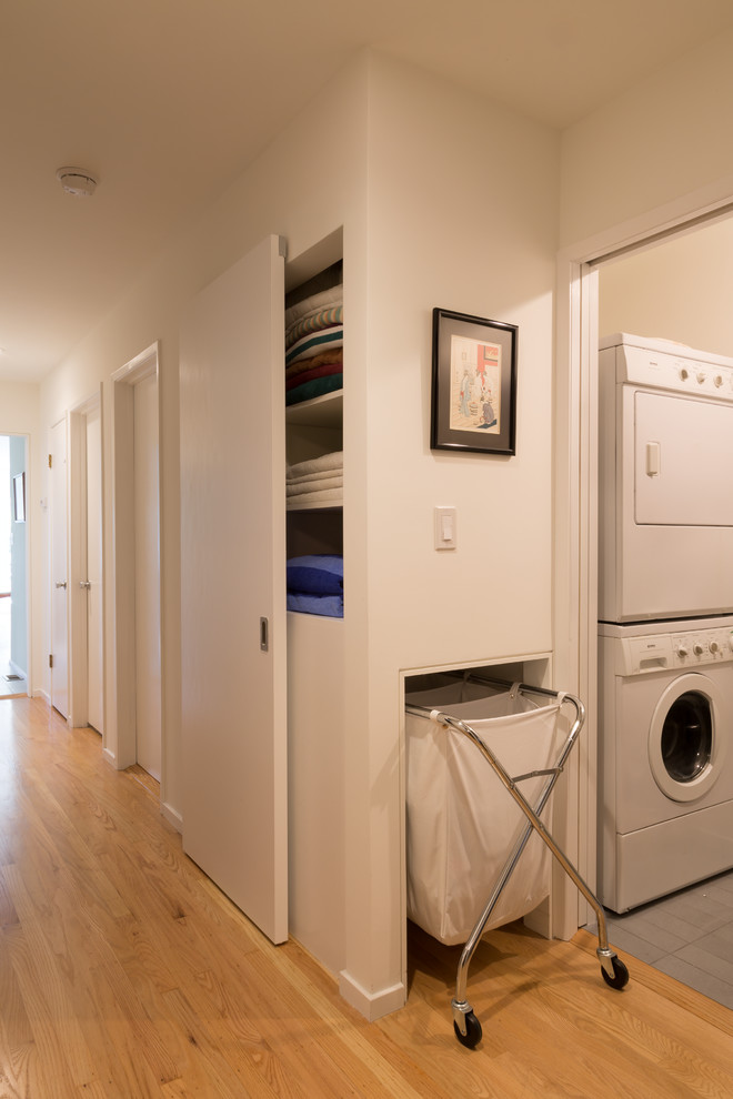 This is an example of a small midcentury utility room in San Francisco with white walls, porcelain floors and a stacked washer and dryer.