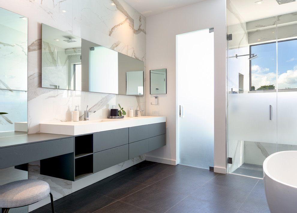 Design ideas for a contemporary bathroom in Miami with flat-panel cabinets, grey cabinets, a freestanding tub, a curbless shower, white tile, white walls, a console sink, grey floor, a hinged shower door and white benchtops.