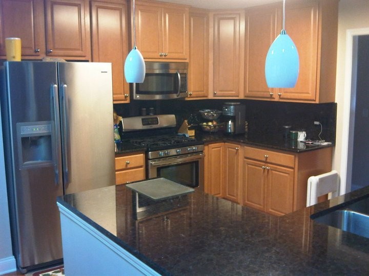 Inspiration for a mid-sized u-shaped enclosed kitchen remodel with a double-bowl sink, raised-panel cabinets, medium tone wood cabinets, granite countertops, black backsplash, stone slab backsplash, stainless steel appliances and a peninsula