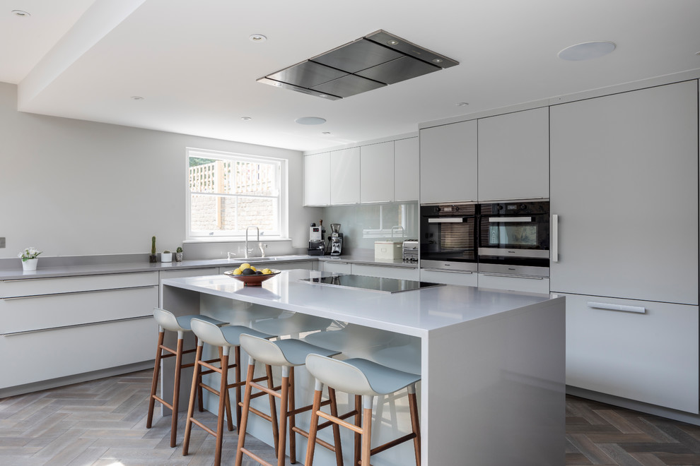 Mid-sized contemporary l-shaped eat-in kitchen in London with an undermount sink, flat-panel cabinets, grey cabinets, grey splashback, glass sheet splashback, stainless steel appliances, dark hardwood floors, a peninsula and brown floor.
