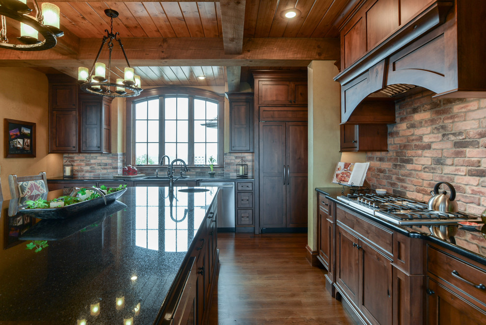 Photo of a mid-sized country l-shaped eat-in kitchen in Other with an undermount sink, shaker cabinets, medium wood cabinets, brick splashback, stainless steel appliances, with island and brown floor.