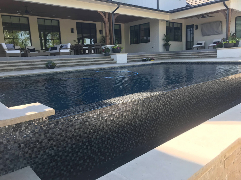 Ejemplo de piscina infinita retro grande rectangular en patio trasero con privacidad y suelo de hormigón estampado