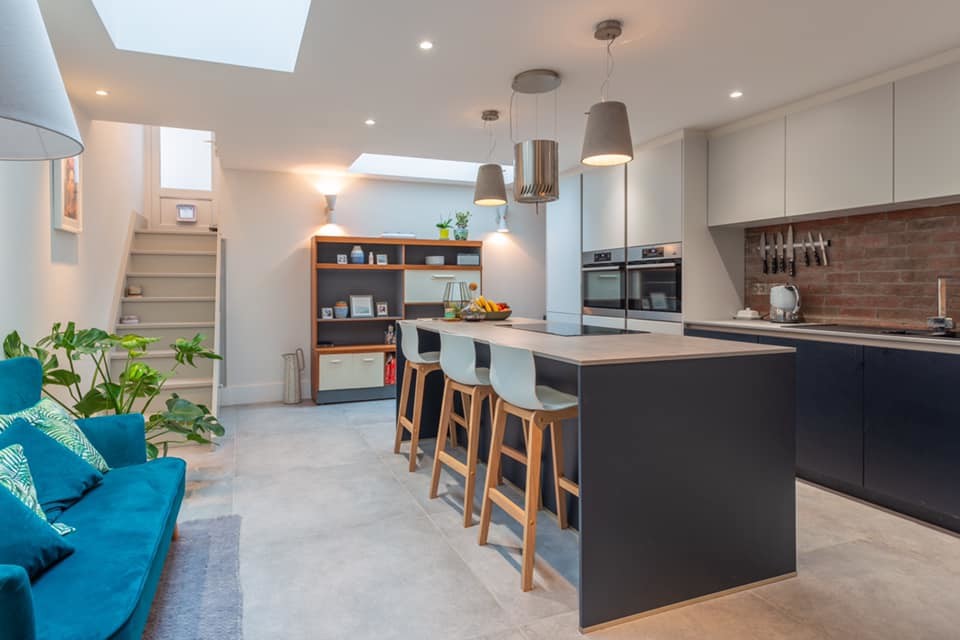 This is an example of a mid-sized modern single-wall eat-in kitchen in Cardiff with an integrated sink, flat-panel cabinets, blue cabinets, concrete benchtops, red splashback, brick splashback, stainless steel appliances, concrete floors, with island, grey floor and grey benchtop.