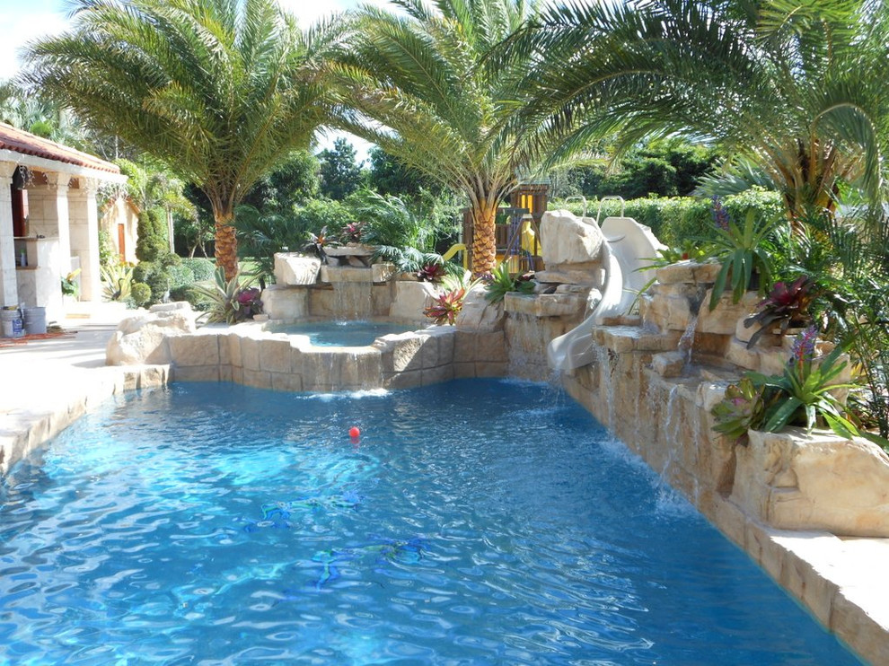 This is an example of a large tropical backyard custom-shaped natural pool in Tampa with a water slide and brick pavers.