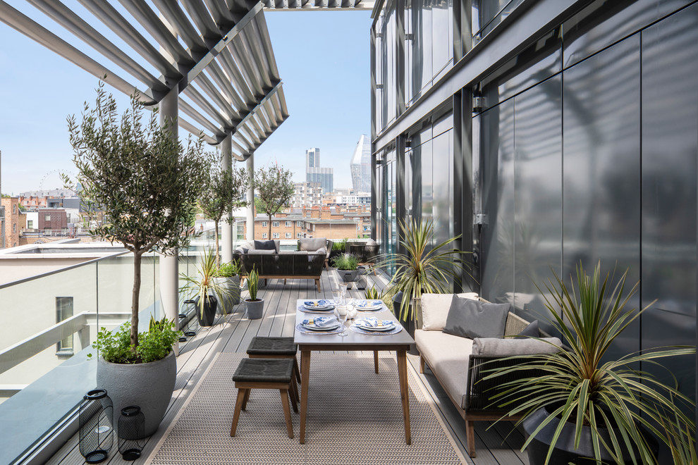 Expansive contemporary balcony in London with a container garden, a pergola and glass railing.