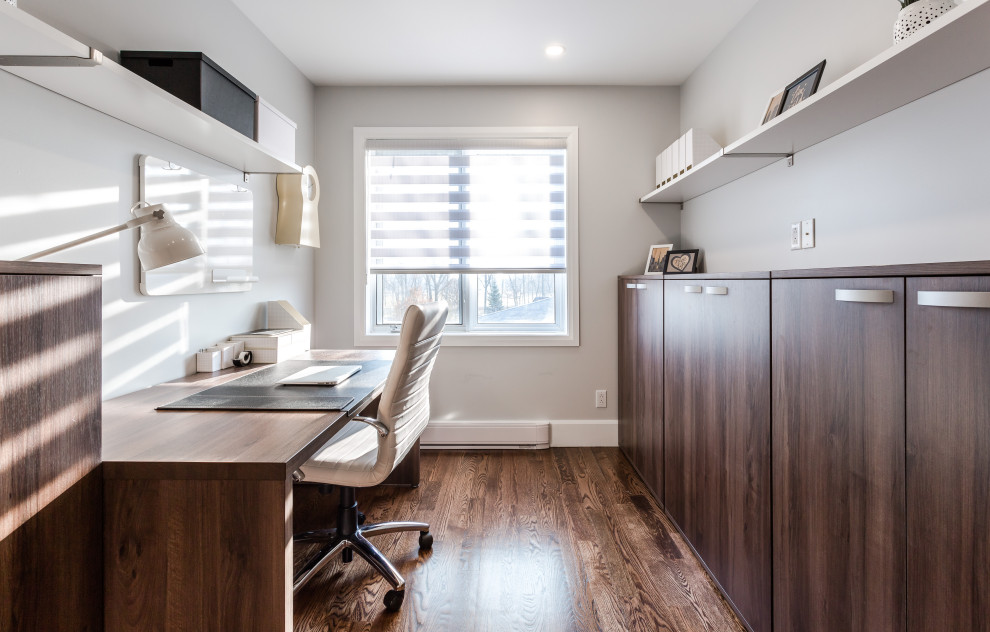 Mittelgroßes Modernes Arbeitszimmer mit Arbeitsplatz, grauer Wandfarbe, braunem Holzboden, freistehendem Schreibtisch und braunem Boden in Montreal
