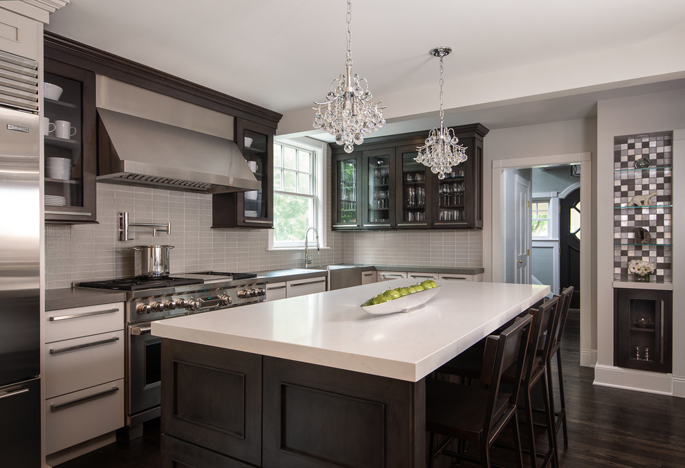 Photo of a mid-sized contemporary l-shaped eat-in kitchen in Birmingham with quartz benchtops, grey splashback, glass tile splashback, stainless steel appliances, dark hardwood floors, with island, flat-panel cabinets, dark wood cabinets, brown floor, white benchtop and a farmhouse sink.