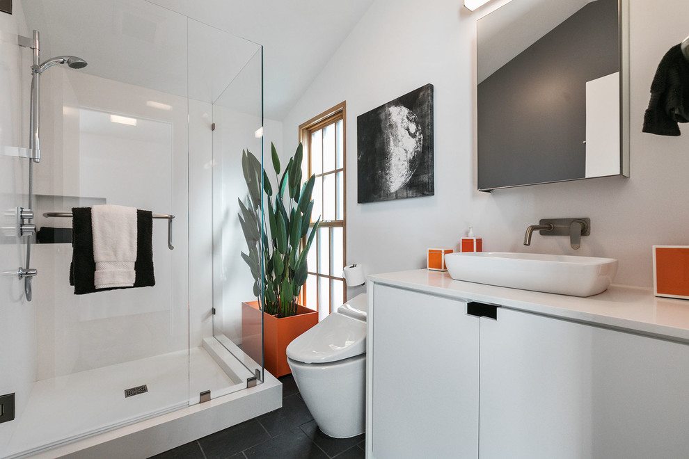 This is an example of a contemporary 3/4 bathroom in San Francisco with flat-panel cabinets, a corner shower, a one-piece toilet, white tile, stone slab, white walls, a vessel sink, engineered quartz benchtops, a hinged shower door, white benchtops, white cabinets, slate floors and black floor.