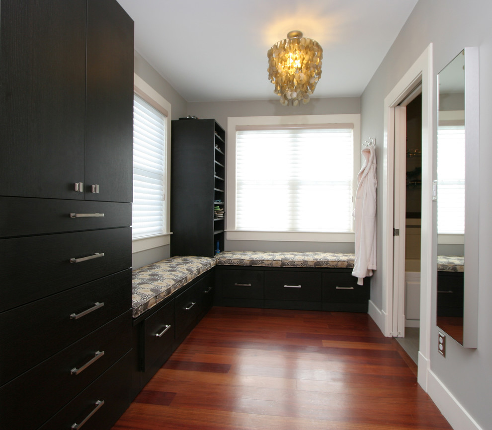 Photo of a mid-sized transitional gender-neutral walk-in wardrobe in Boston with flat-panel cabinets, black cabinets, medium hardwood floors and brown floor.