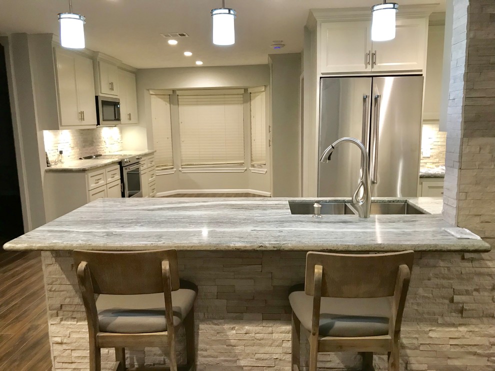 Inspiration for a large transitional u-shaped porcelain tile and brown floor eat-in kitchen remodel in Houston with an undermount sink, shaker cabinets, white cabinets, granite countertops, white backsplash, stone tile backsplash, stainless steel appliances and a peninsula