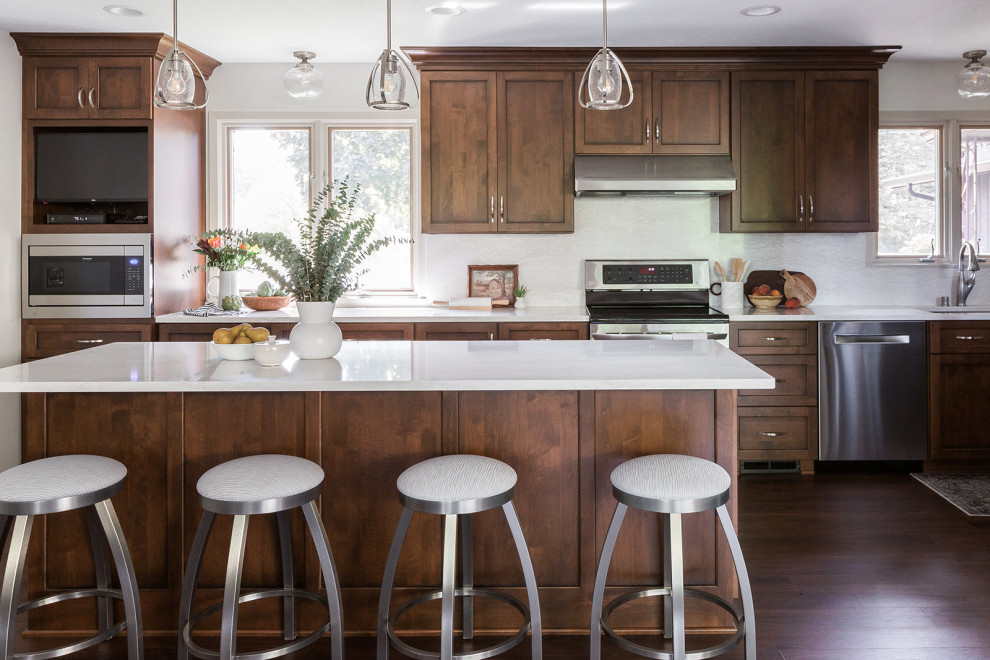 Large transitional galley brown floor and dark wood floor kitchen photo with an undermount sink, shaker cabinets, quartz countertops, white backsplash, quartz backsplash, stainless steel appliances, an island, white countertops and dark wood cabinets